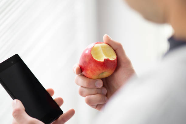 istock male hand holding bitten apple and smartphone selective focus on the apple, man eating apple while working on his phone 2154351884