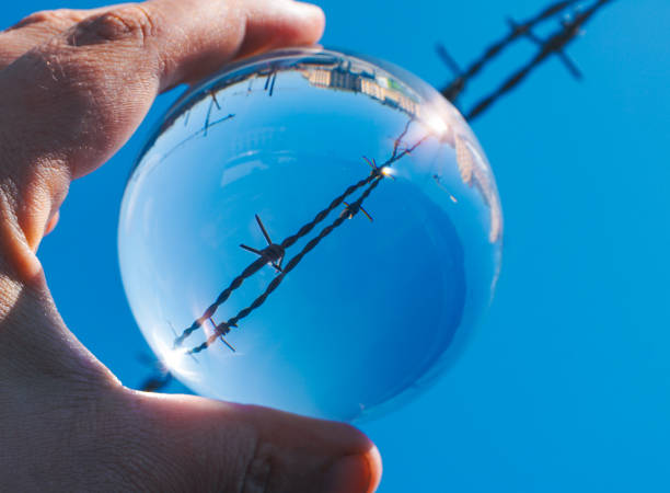 Cropped hand holding a crystal ball against a barbed wire