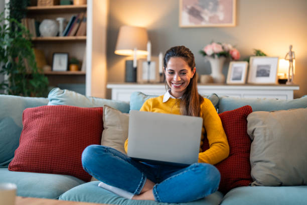 istock Pretty young woman working with her laptop while sitting on couch at home 2154359778