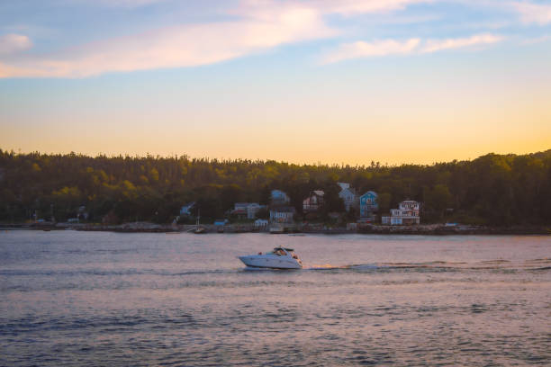Boat setting out on the ocean, cruising past houses located in Purcell's Cove / Purcells Cove, a community in Halifax, Nova Scotia. This view can be seen from Point Pleasant Park.