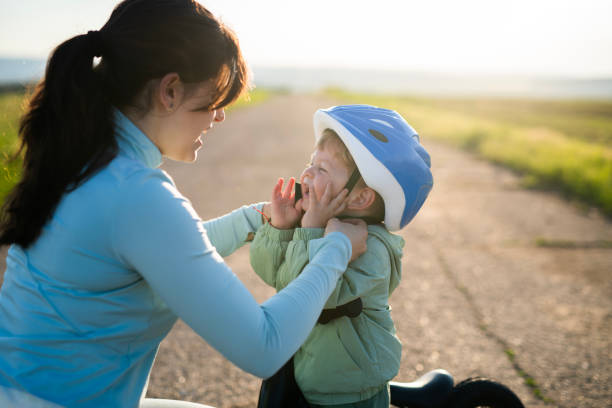 Safety first during bike riding lessons with mom. Mother adjusting her little boy's helmet.
