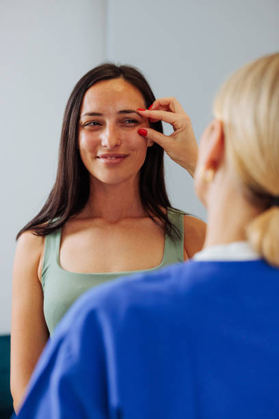 istock Woman smiling while dermatologist examines the skin on her face 2154373733