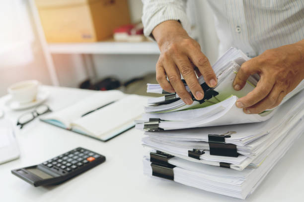 istock A busy office worker checking and organizing a large pile of documents at their desk. 2154380823