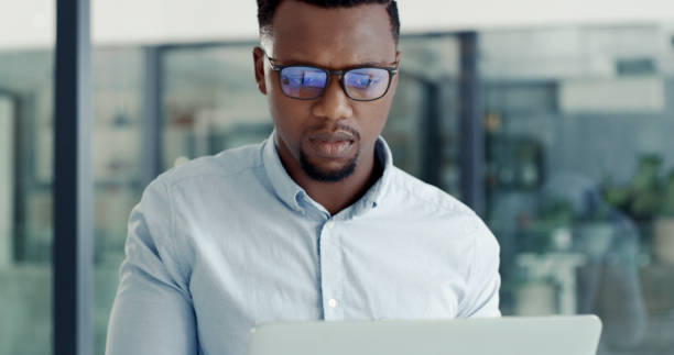 istock Focused young business man using a laptop in a modern office. A serious businessman working online at his desk 2154381276