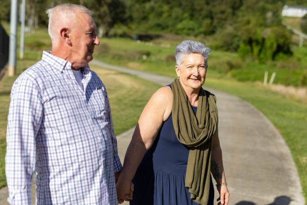Elderly couple walking in the park talking laughing . Senior woman blind and her husband helping her to walk. Senior couple spending time in nature. Old mature supposes enjoying outdoors retirement.