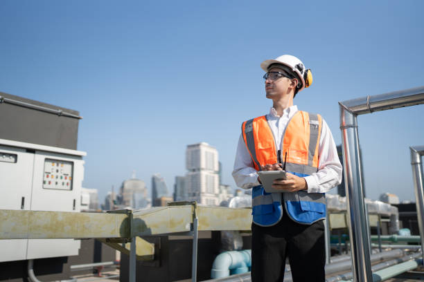istock Portrait Asia male engineer in protective workwear is performing a conducts system check with use tablet computer and walkie talkie at rooftop building 2154395983