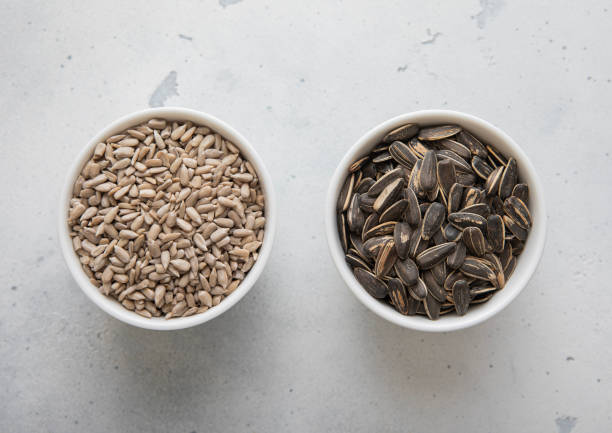 istock Whole and peeled healthy sunflower seeds in ceramic bowl plates on light kitchen table.Macro. 2154400546