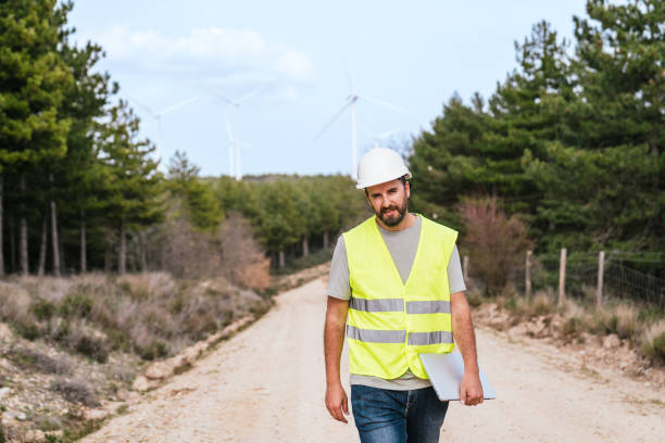 istock Technician in High-Visibility Vest Walking Near Wind Turbines in Forested Area 2154406834