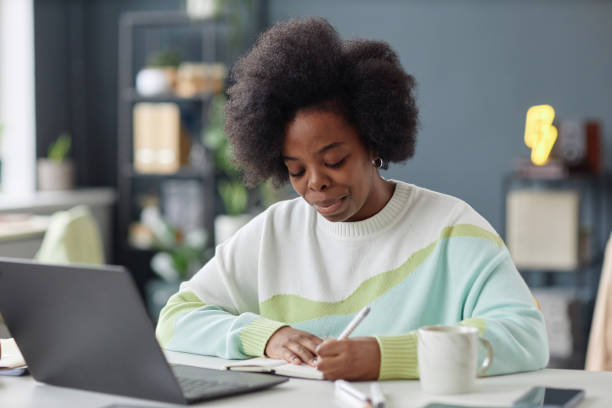istock Black Woman Sitting at Desk in Office Writing 2154415691
