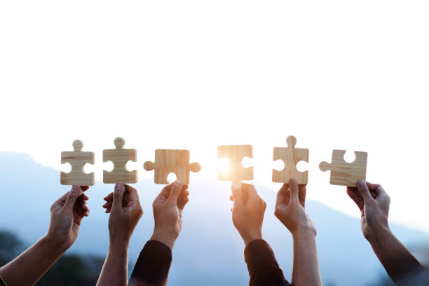 Teamwork and partnership concept. Hands are raised against a bright, white sky, each holding a piece of a wooden jigsaw puzzle. teamwork, problem-solving, Charity, volunteer. Unity, team business.