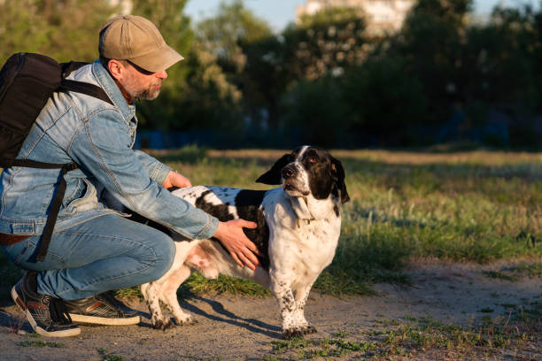 Young man crouching on the ground, affectionately petting his German Shepherd dog in a rural park setting