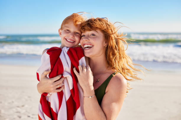 istock Lovely woman hugging child with towel at beach while smiling 2154428186