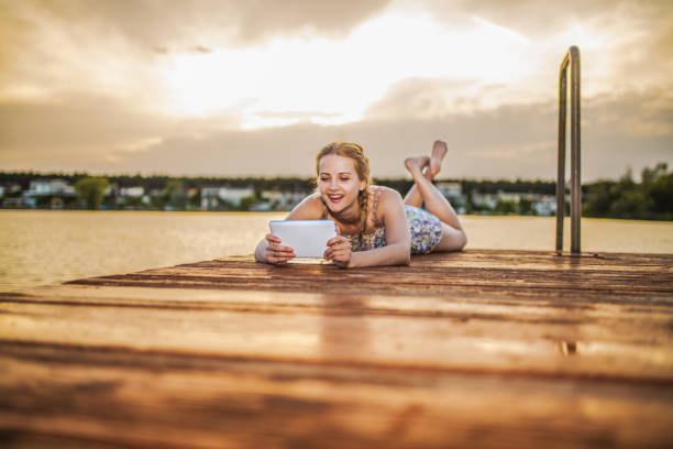 istock Young woman using digital tablet while sitting by the lake at sunset 2154439121
