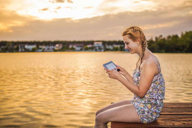 Young woman using digital tablet while sitting by the lake at sunset