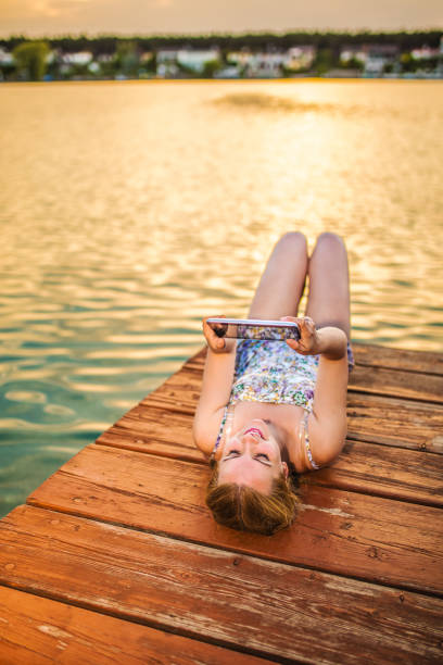 Young woman using digital tablet while sitting by the lake at sunset