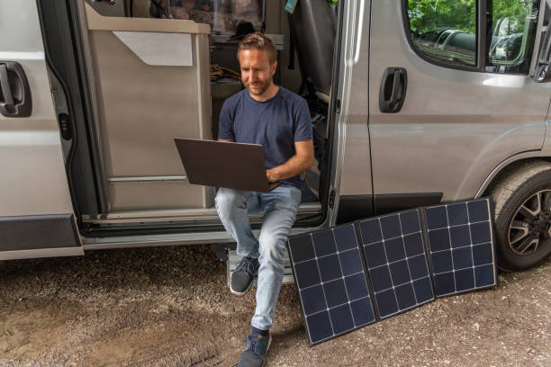 istock Remote working, Man uses laptop powered with a solar panel from his camper van 2154441124