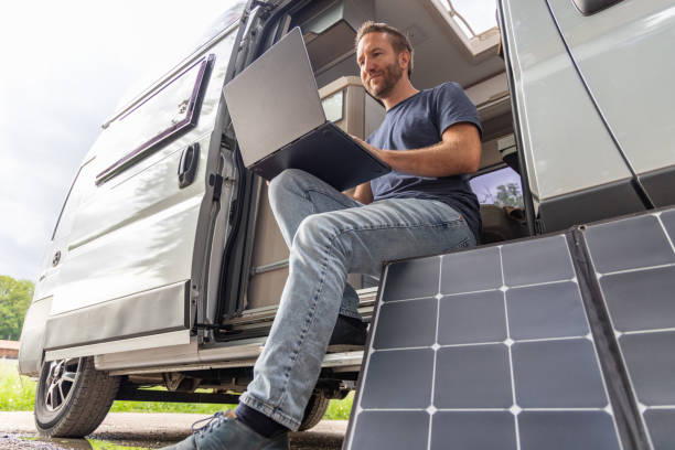 istock Remote working, Man uses laptop powered with a solar panel from his camper van 2154441163