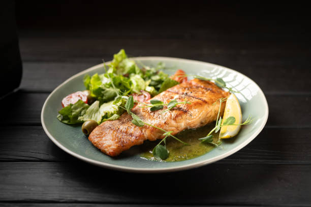 istock Seared salmon steak with lemon slices and vegetables served on blue plate 2154451206
