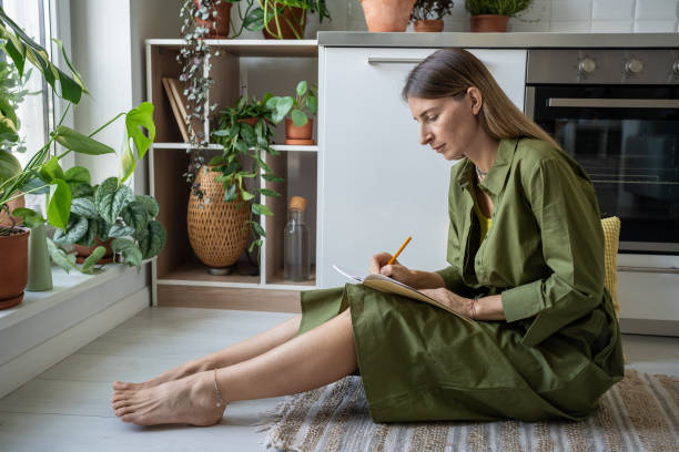 istock Serious attentive woman focused on notebook writing personal diary sitting on kitchen floor at home. 2154451764