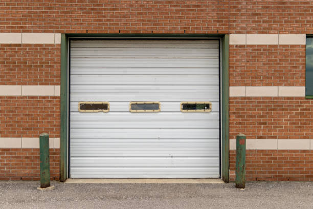 istock Closed white garage door set into red brick wall - patterned with lighter bricks - green bollards and concrete ground 2154461250
