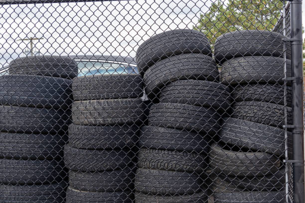 Used tires stacked high - visible through chain-link fence - under gray overcast sky. Taken in Toronto, Canada.