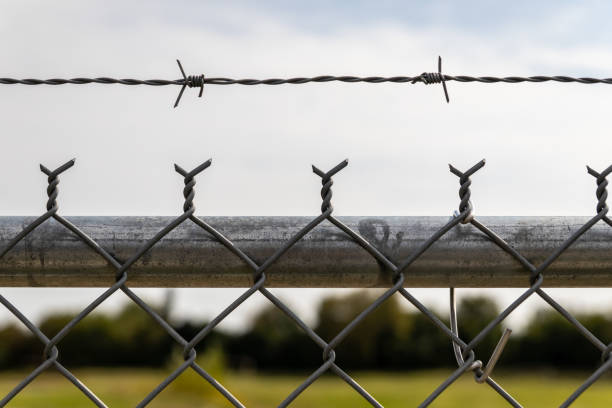 Barbed wire fence - clear sky backdrop - security boundary - restricted area - minimal cloud cover. Taken in Toronto, Canada.