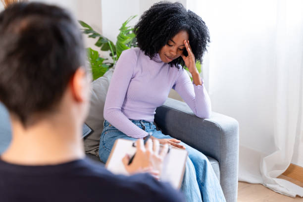 istock Young woman talks about her feelings while sitting on a couch, with a therapist taking notes in the foreground 2154468350