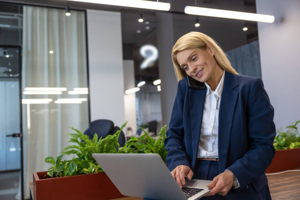 istock Businesswoman calling talking on mobile phone while working on laptop in office 2154472044