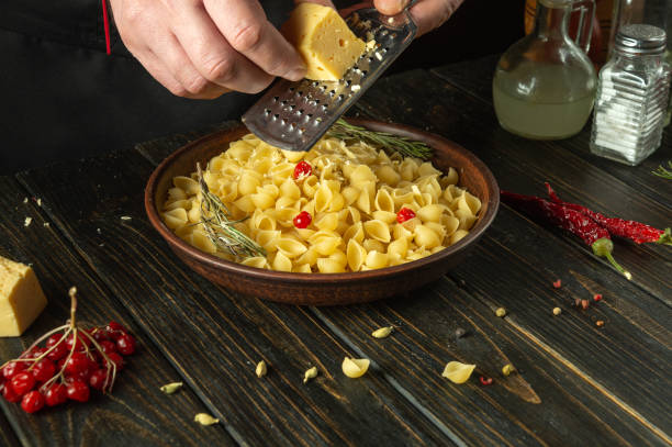 istock The chef adds hard cheese to a plate of pasta using a grater. Working environment on the kitchen table in the cook room. Delicious pasta with vegetables and aromatic spices 2154472063