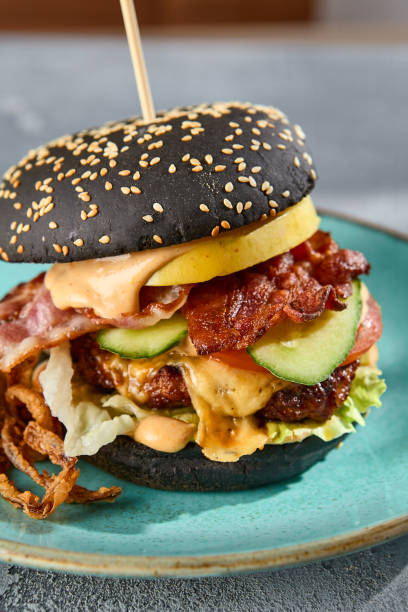 istock Gourmet black burger with bacon and crispy onions on a turquoise plate, gray textured backdrop with a hint of sunlight 2154475268