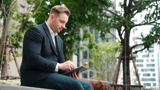 istock Businessman sitting at park while working on tablet by reading report. Urbane 2154476695