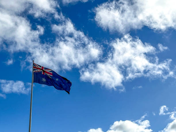 Australian flag against blue sky with puffy clouds