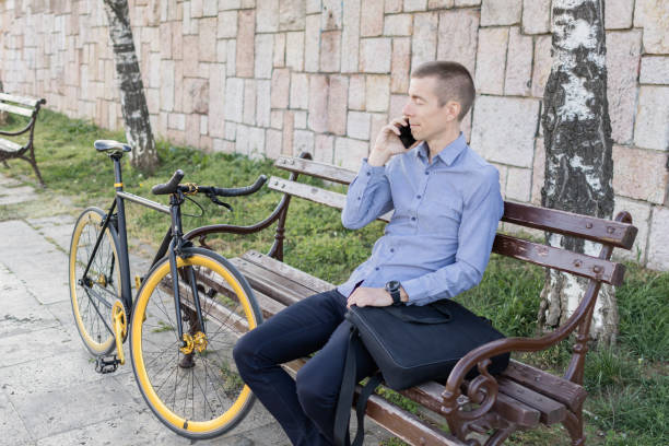 istock Smiling businessman commuter using mobile phone. He is enjoying at public park on his bicycle trip from work after a long workday. Sustainable concept of going to work by bicycle. 2154497722
