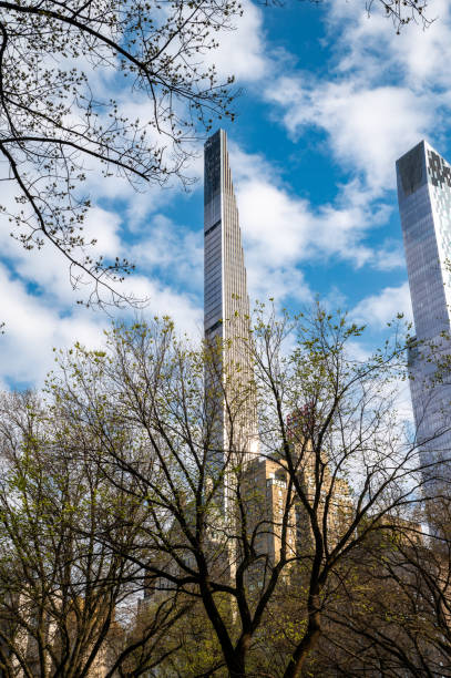 NYC's Art Deco gem basks in sunshine! Steinway Tower rises above lush greenery in Central Park in a sunny day and some trees in the foreground. Ideal for travel & architecture content.