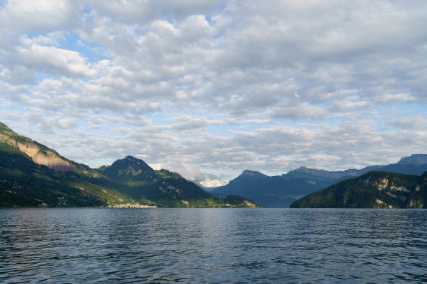 White passenger ferry with Swiss flag cruising on calm lake waters. Scenic mountain landscape with cloudy sky in the background. Boat transportation and travel on Swiss lakes.