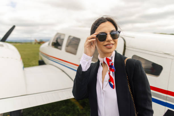 A stylish woman stands confidently next to a large airplane on a runway during sunset. The warm light highlights her outfit and the aircraft s details.