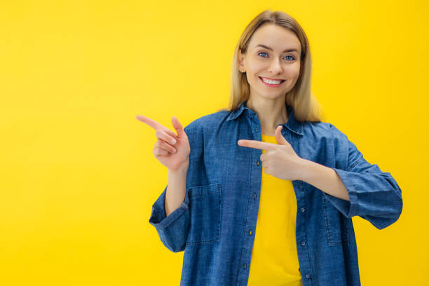 istock Smiling beautiful young woman look camera pointing fingers hands on copy space workspace isolated on yellow background in studio 2154525542