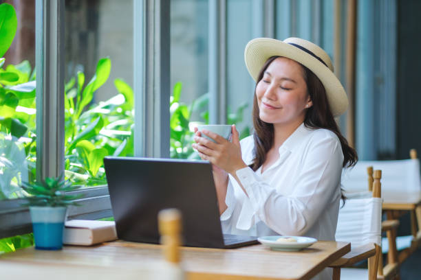istock Portrait image of a young woman with hat drinking coffee while working on laptop computer in cafe 2154546155