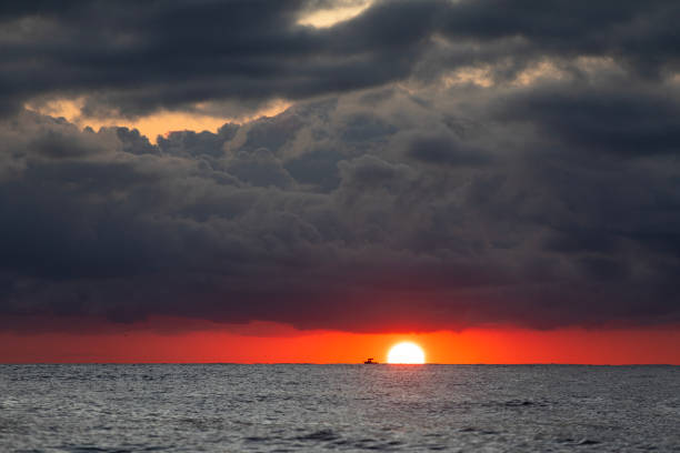 Orange sunrise with dramatic storm clouds over the ocean and a fishing boat on the horizon