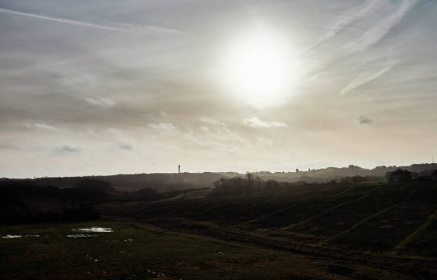 Scenic view of grassy landscape and silhouette mountain range against bright sun in cloudy sky during sunny day