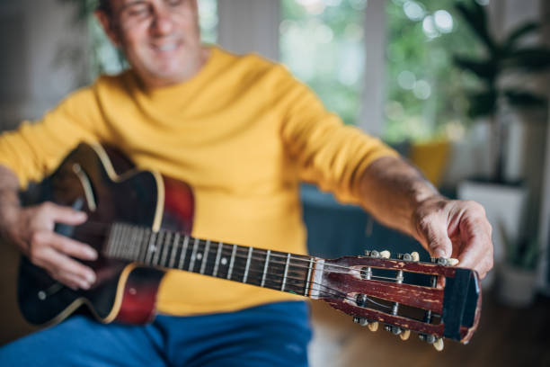 Happy elderly man with a guitar, tuning the instrument and preparing to play music, expressing joy and leisure in his hobby
