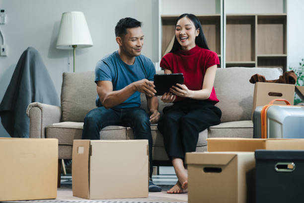 istock Young couple relaxing sitting on the sofa using the computer laptop around cardboard boxes, very happy moving to a new house. 2154603171