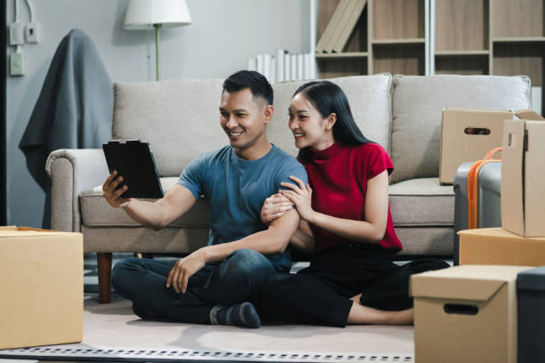 istock Young couple relaxing sitting on the sofa using the computer laptop around cardboard boxes, very happy moving to a new house. 2154603181