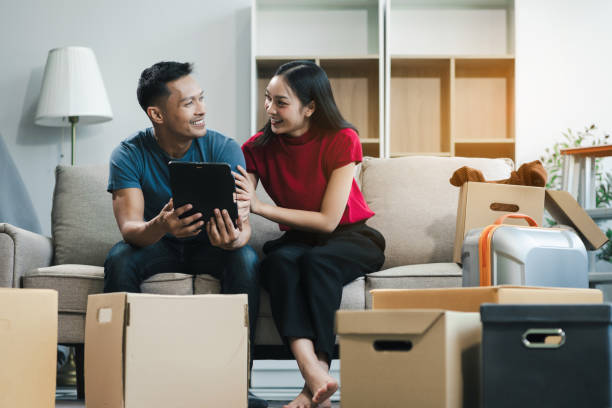 istock Young couple relaxing sitting on the sofa using the computer laptop around cardboard boxes, very happy moving to a new house. 2154603182