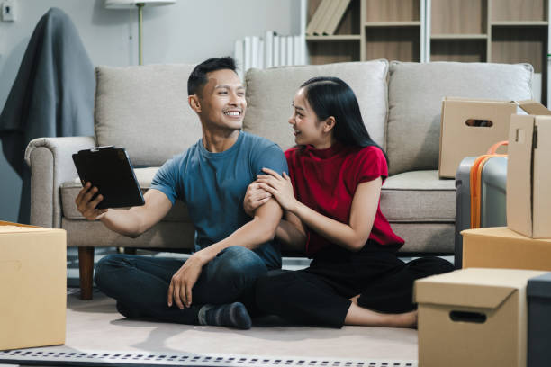istock Young couple relaxing sitting on the sofa using the computer laptop around cardboard boxes, very happy moving to a new house. 2154603185
