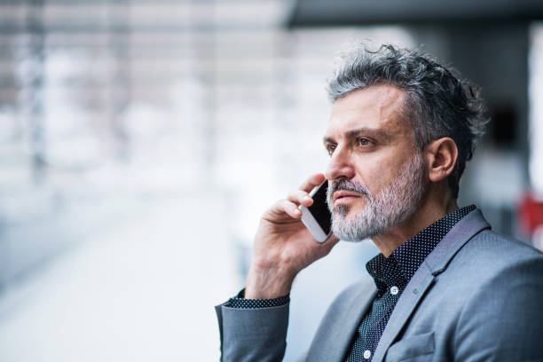 istock Handsome businessman standing in modern office hallway, making phone call. 2154603614