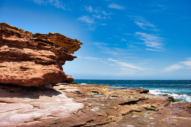 Heavily eroded red-brown sandstone cliffs and rock plateau with rock pools at the coast of Kalbarri National Park, Western Australia.