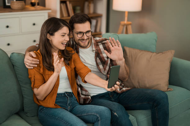 istock Happy couple using phone for a video call while relaxing on sofa at home. 2154610192