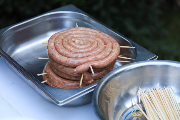 Raw spiral sausage in a metal tray with skewers, ready for grilling, displayed outdoors