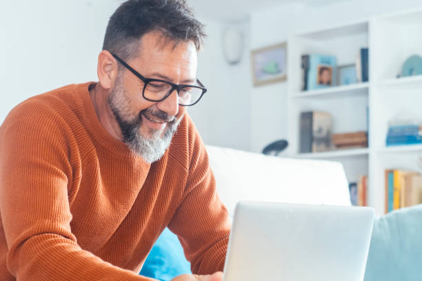 istock One mature man alone at home using laptop sitting on sofa smiling and enjoying wireless technology and computer connection. Small business and alternative office modern people lifestyle. Male beard 2154620988